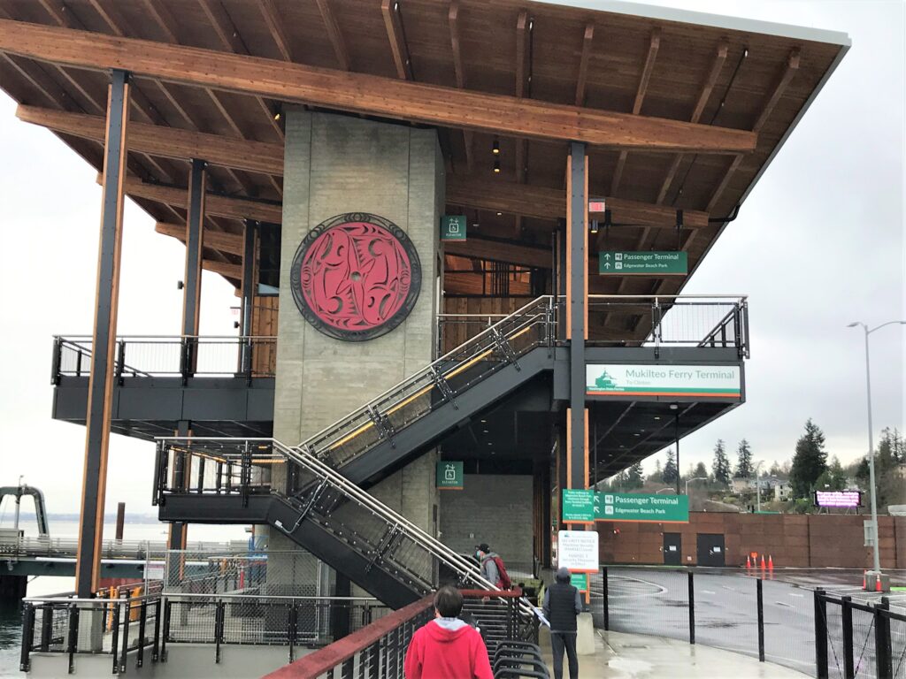 a side view of the new ferry terminal shows the stairs, wood roof, and a concrete pillar with tribal artwork