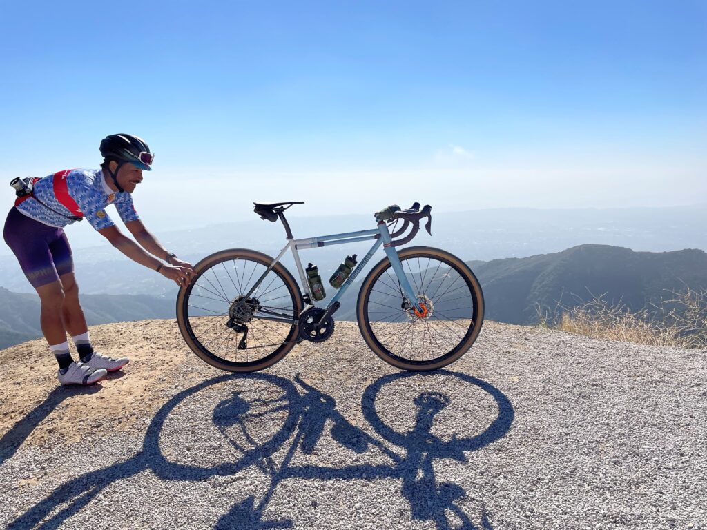 A person holds a bike at the top of a mountain with blue sky in the background