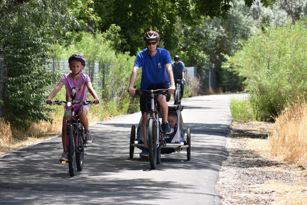 An adult and children biking along a paved trail on a sunny day