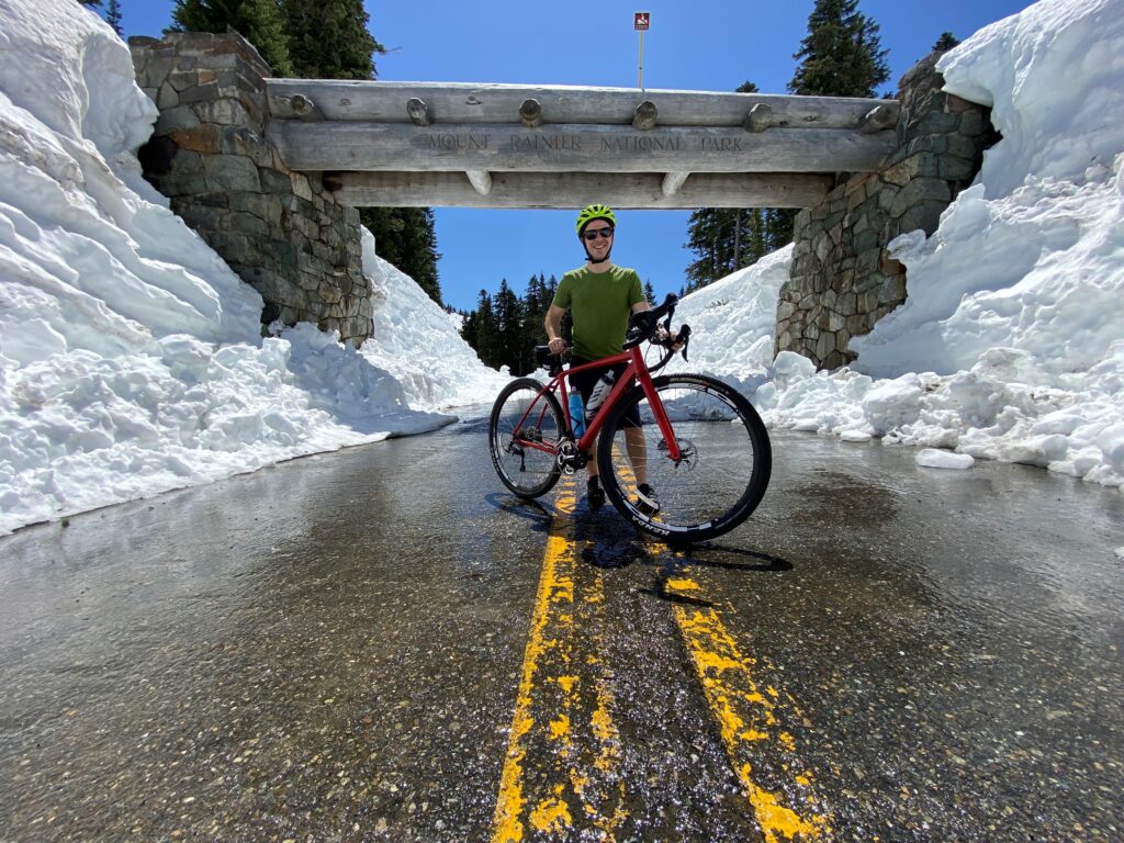 A person stands in front of a wooden entrance on a wet road with snow on both sides