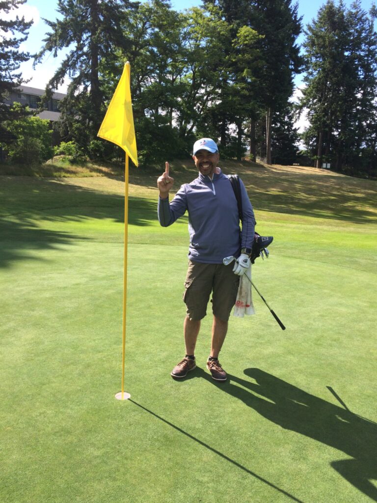 Alvin Valencia on golf course next to hole holding up the number one on his fingers