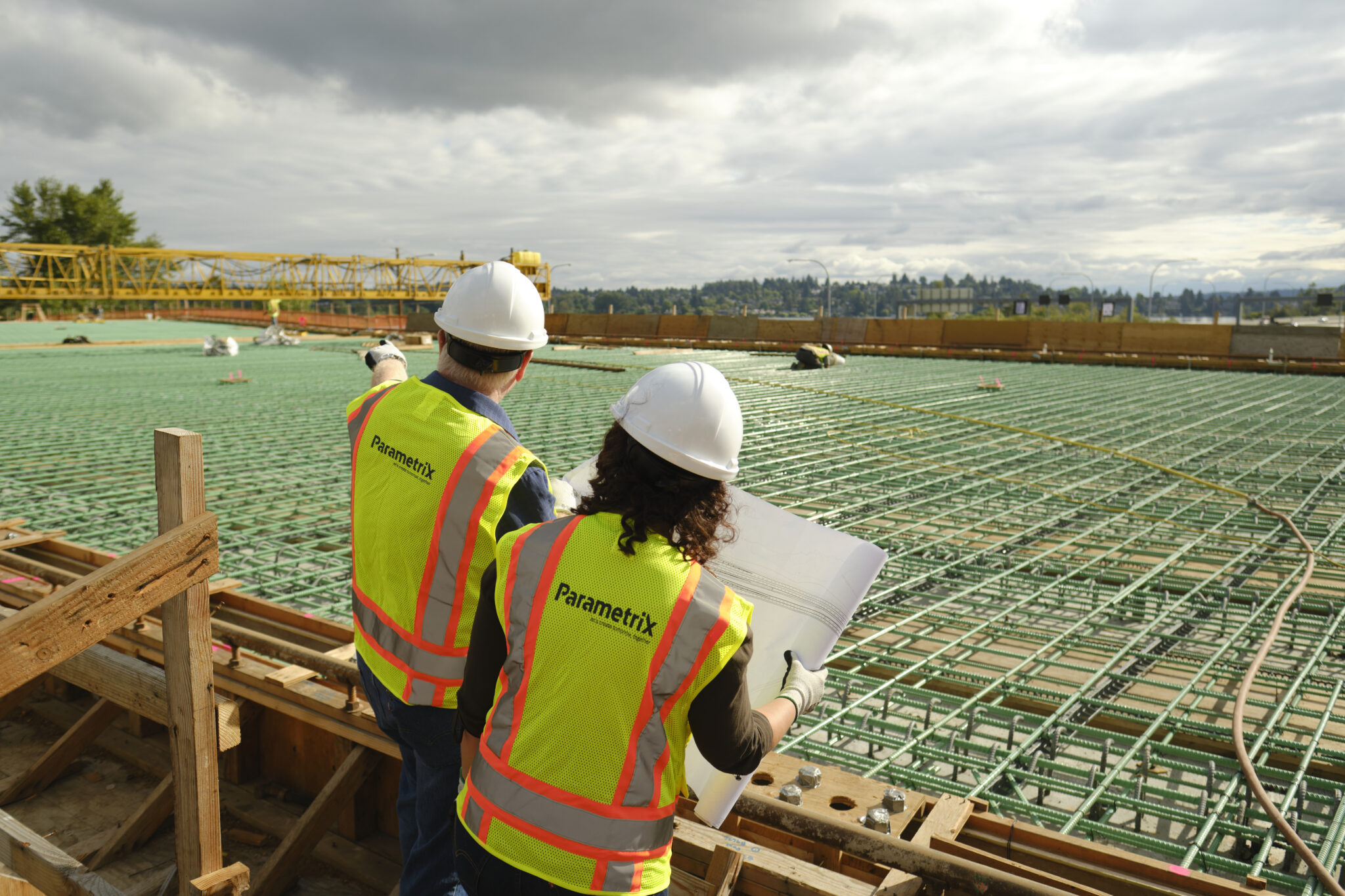 Two people wearing safety vests and hard hats look over a construction site