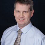 A headshot of a man wearing a shirt and tie