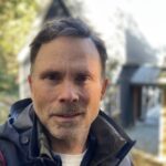 A photo of a man wearing a jacket with a house and trees in the background