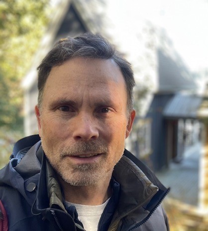 A photo of a man wearing a jacket with a house and trees in the background