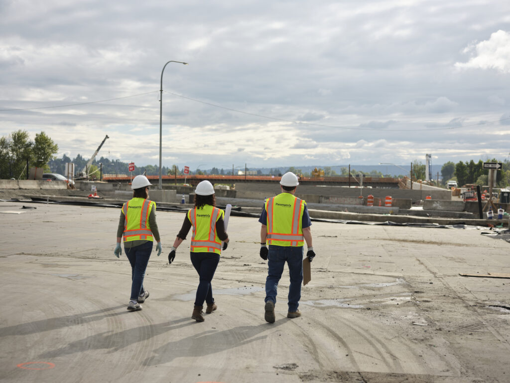 Three people wearing safety vests and hard hats walking away