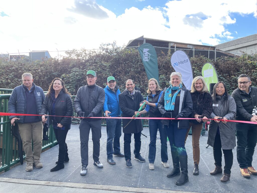 A group of people stands behind a ribbon ready with scissors to cut it.