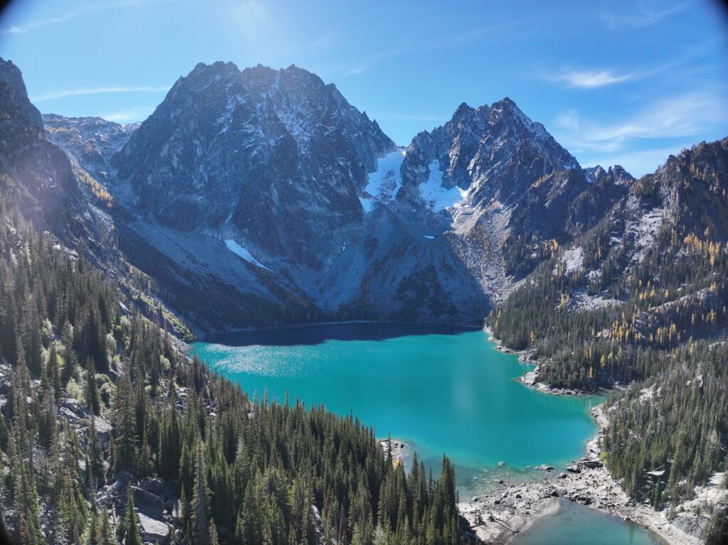 A bird's eye view of a blue lake surrounded by jagged snowy hills