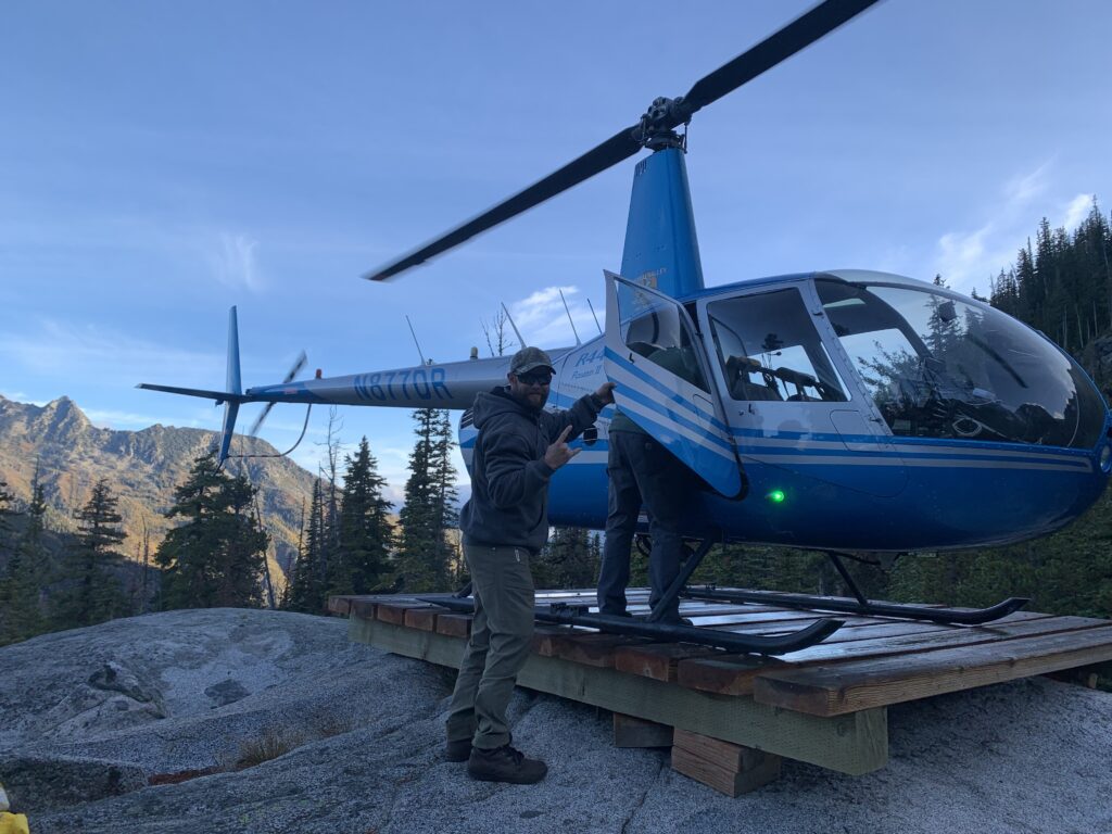 A person gets ready to get into a helicopter on a wooden platform in the mountains