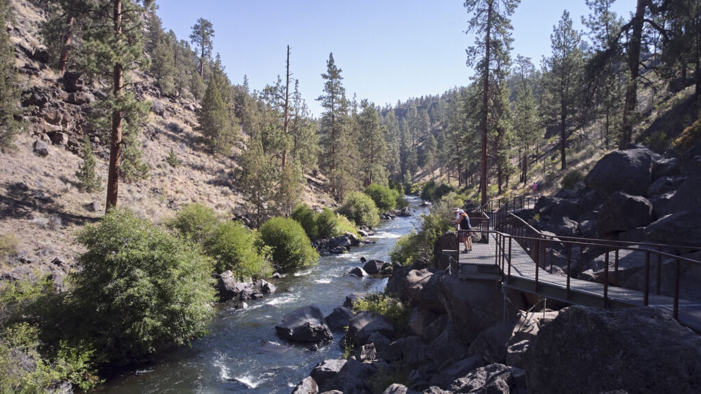 A river winds through a canyon with a pathway on the right.