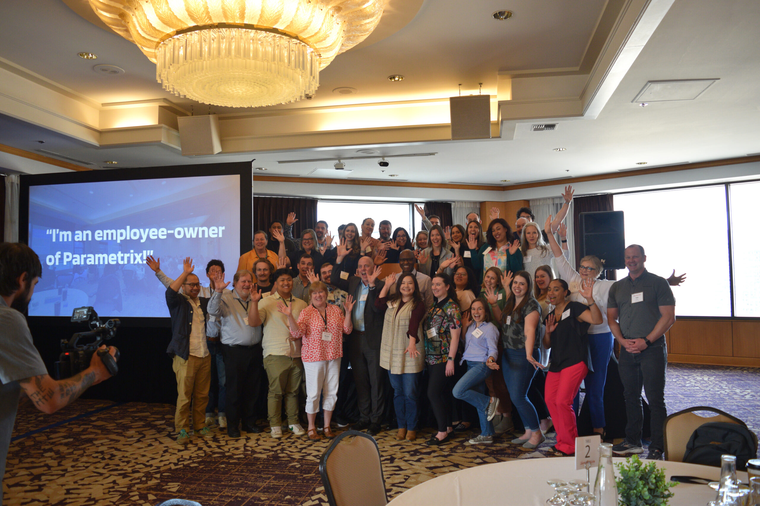 A group of people pose for a photo with their hands up in front of a screen.