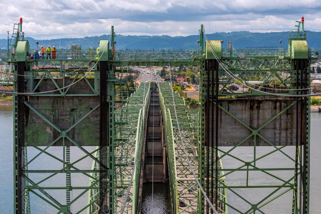 A bird's eye view of a green bridge with workers on the upper deck of the bridge