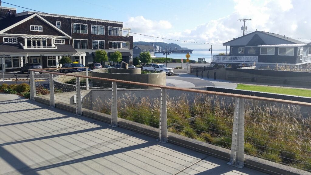 A walkway overlooking vegetation and a spiral rain garden with the Puget Sound in the background