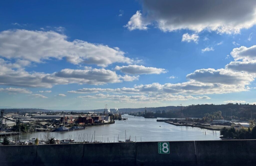 A view from a roadway of a body of water with shipping containers and a marina on the left shore