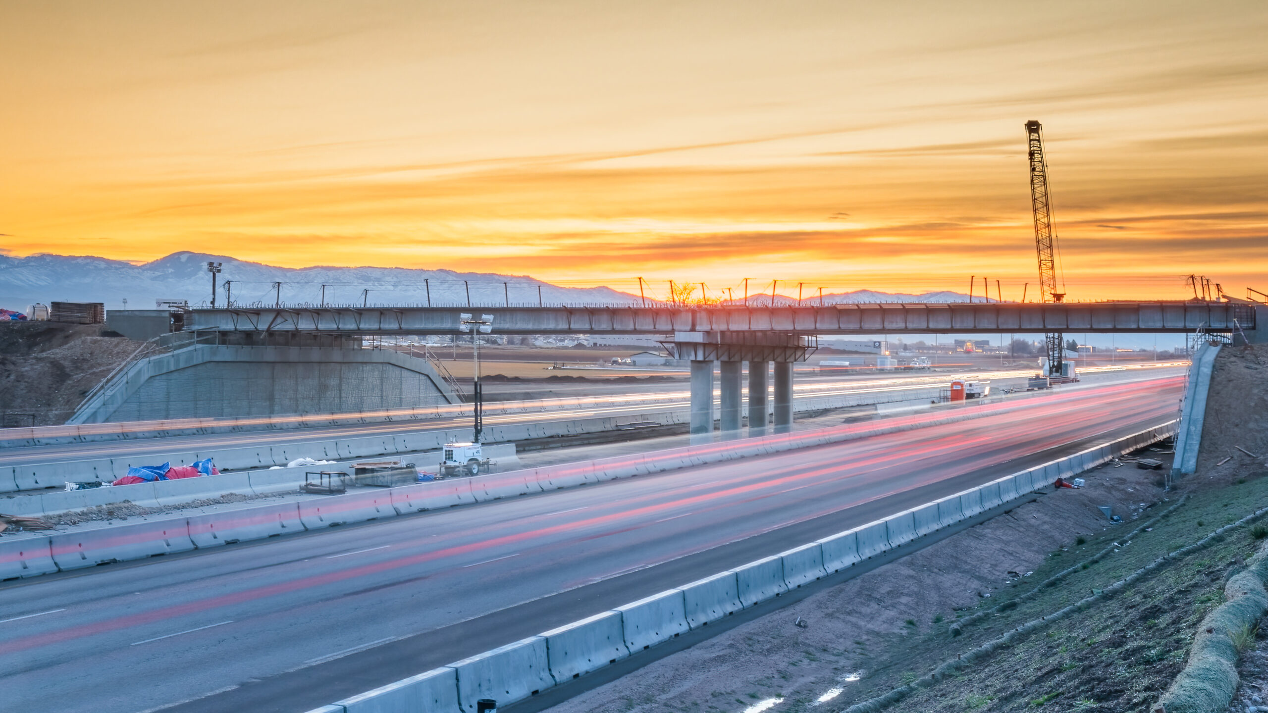 An overpass being constructed over a freeway with the sunset in the background.