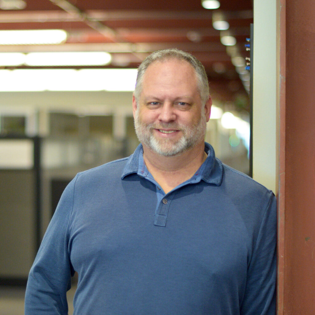 Sean Ryan stands in an office hallway smiling