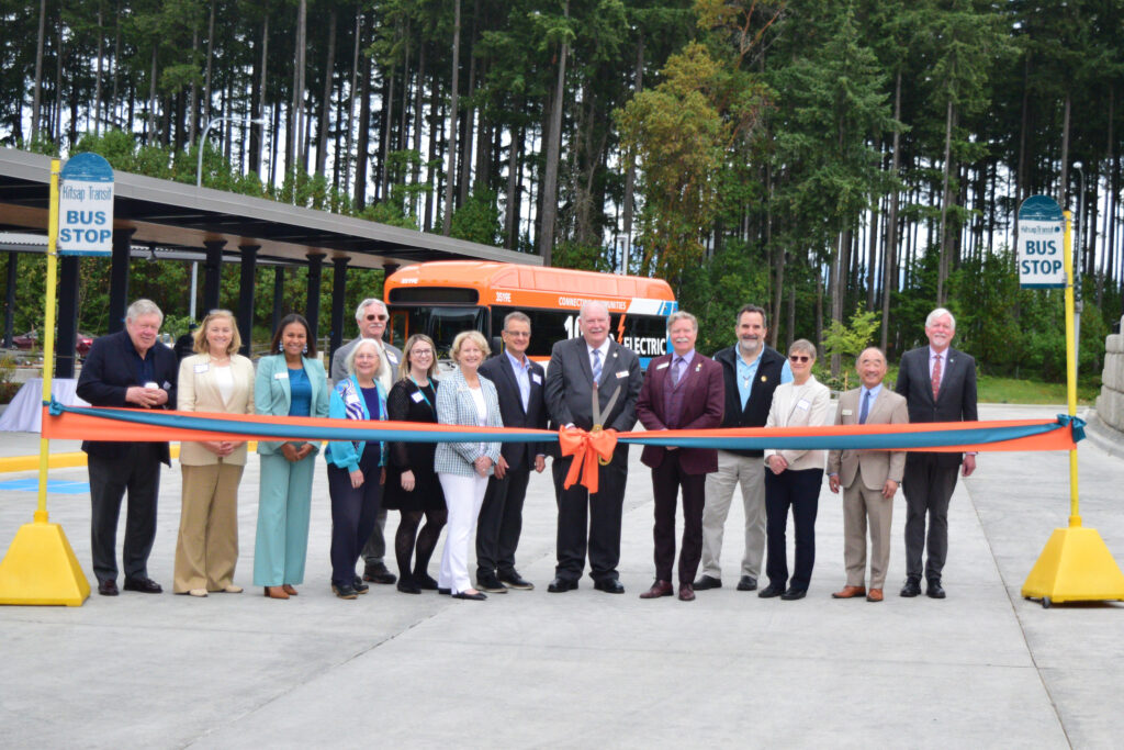 A group of people stand behind a ribbon with a bus in the background.