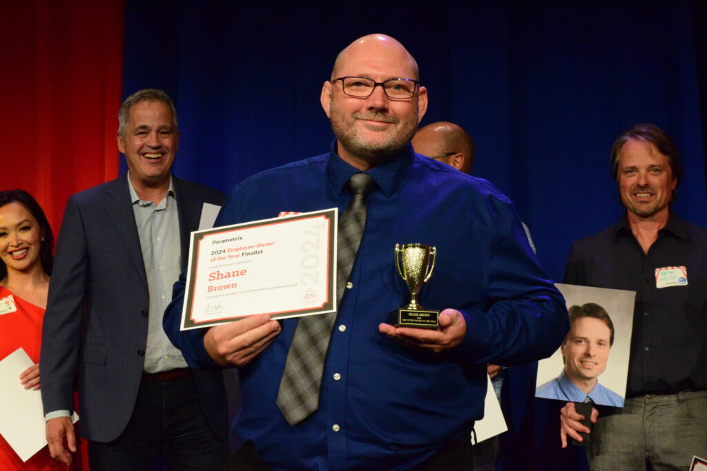 A man holds a certificate and a trophy on a stage.