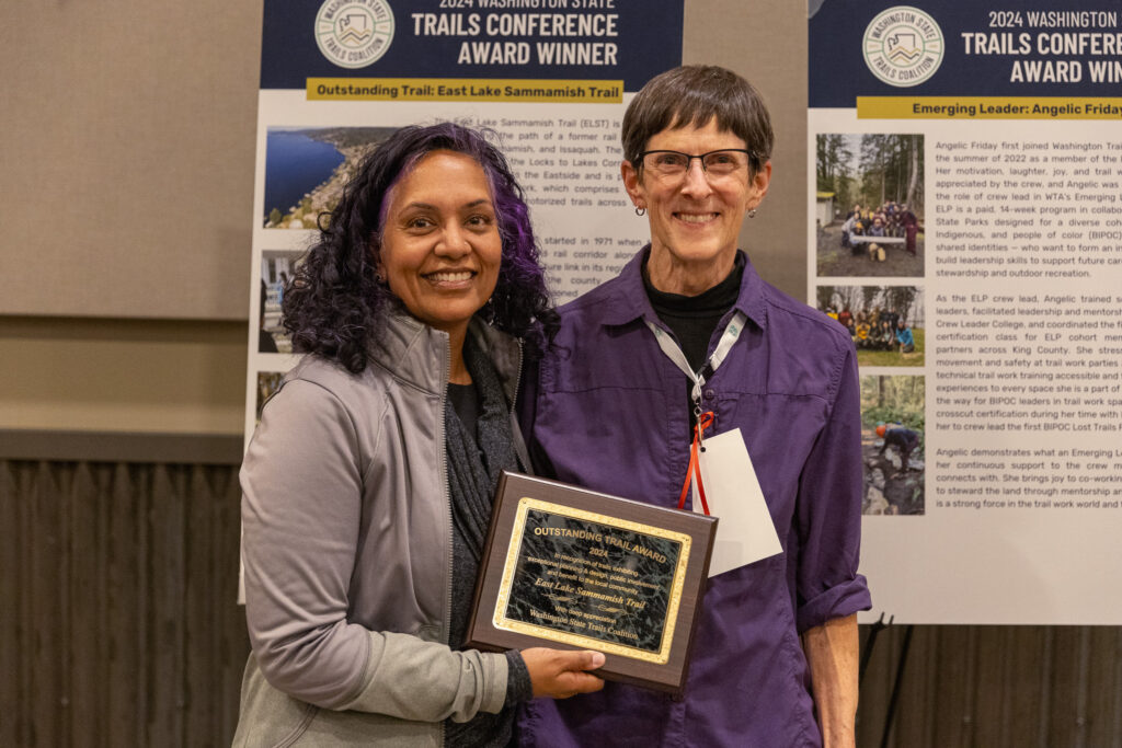 Two people stand in front of a project board holding an award.