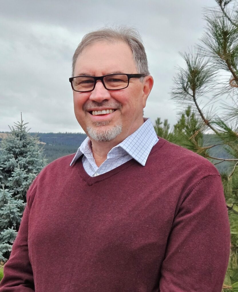 A man in a red sweater and glasses with trees in the background