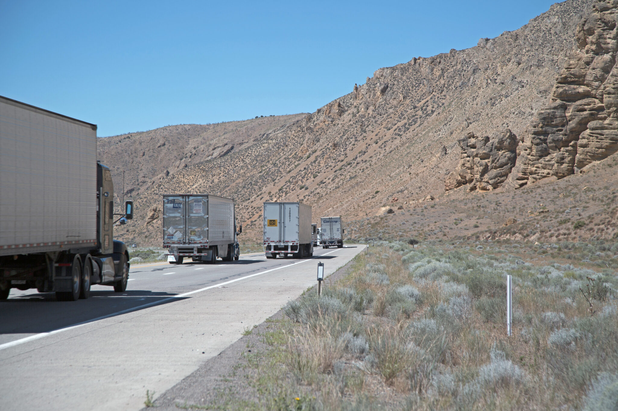 Semi trucks drive along a highway next to a canyon wall