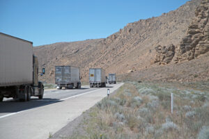 Semi trucks drive along a highway next to a canyon wall