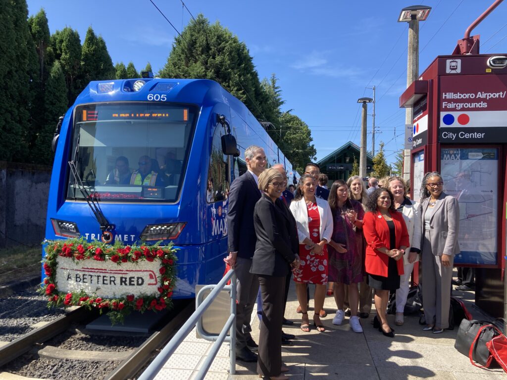A group of people pose in front of a TriMet light rail train with a "A Better Red" sign.