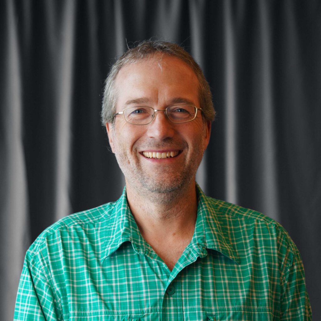 A man in a green checkered shirt smiles for a photoe