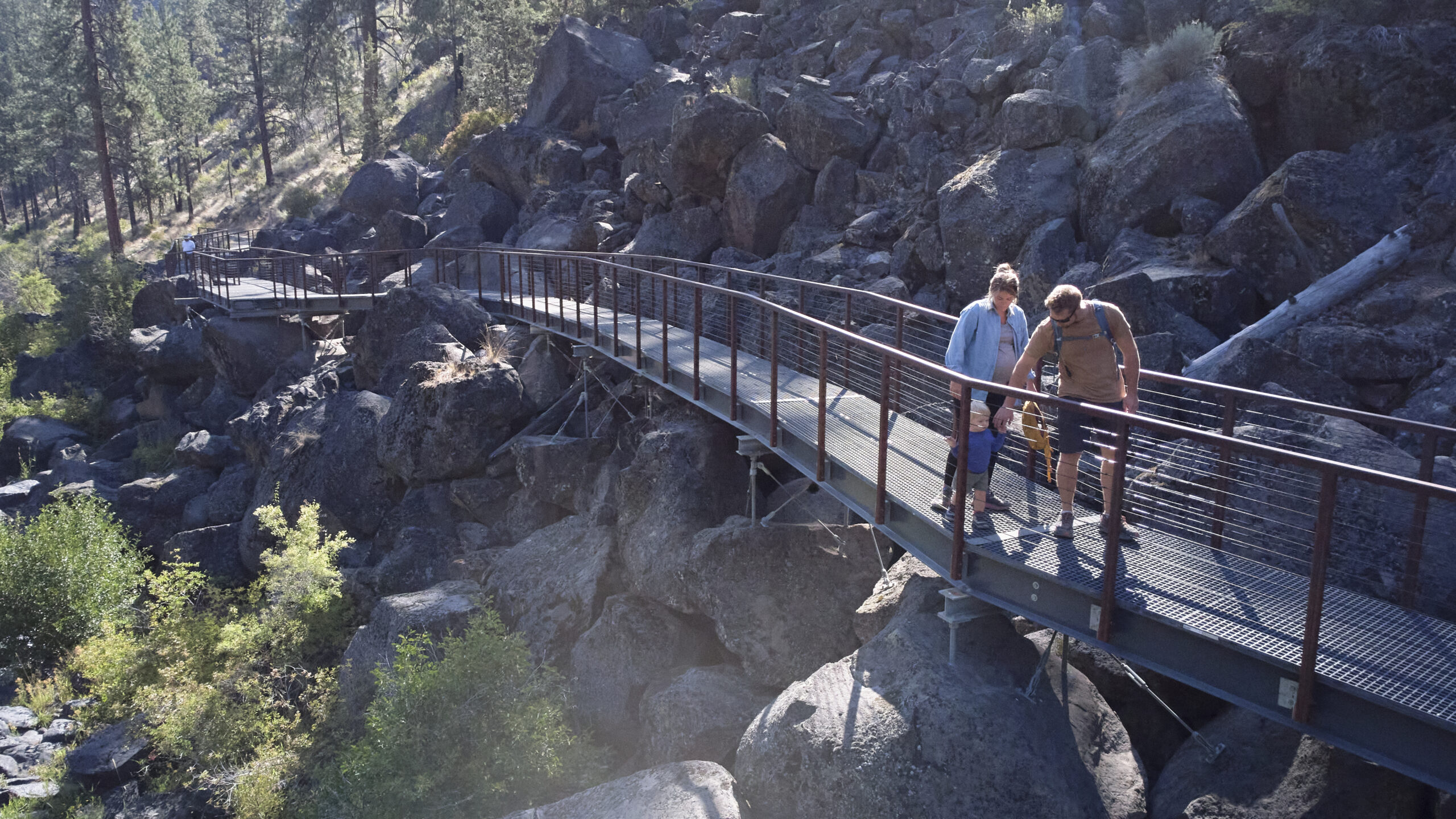 People walk along a pathway surrounded by boulders on one side and a river on the other.