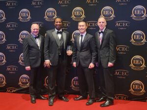 Four people stand in front of a backdrop holding an award