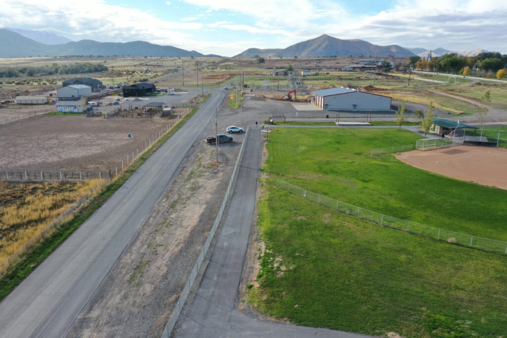 Aerial view of a rural road cutting through farmland with barns, fences, and distant mountains in the background
