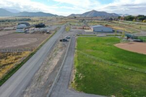 Aerial view of a rural road cutting through farmland with barns, fences, and distant mountains in the background