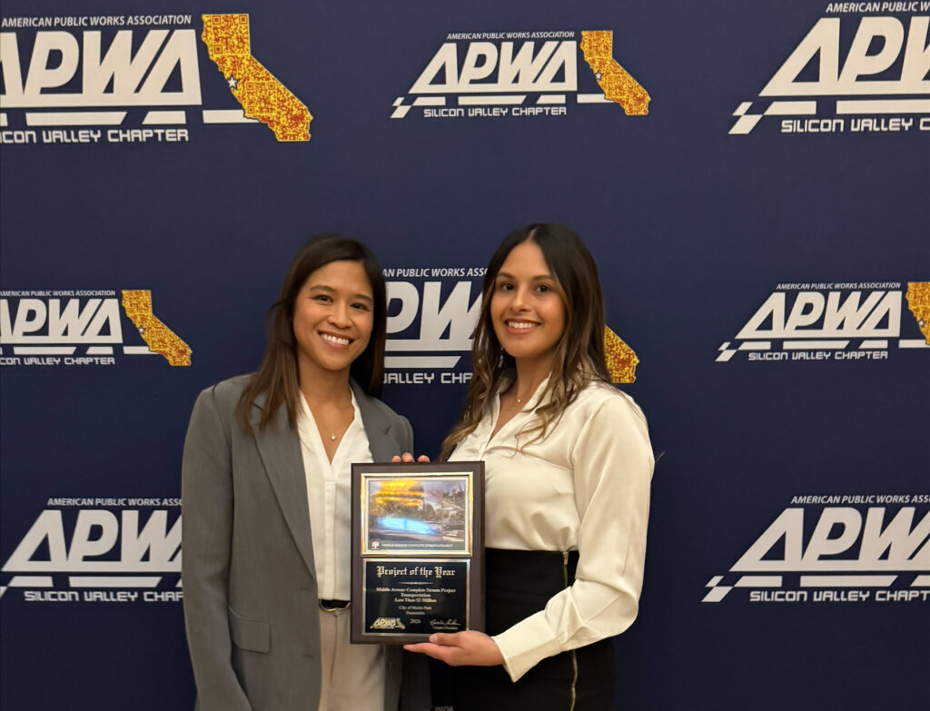 Two women stand in front of a backdrop holding an award plaque