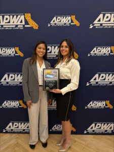 Two people stand in front of a backdrop holding an award plaque.