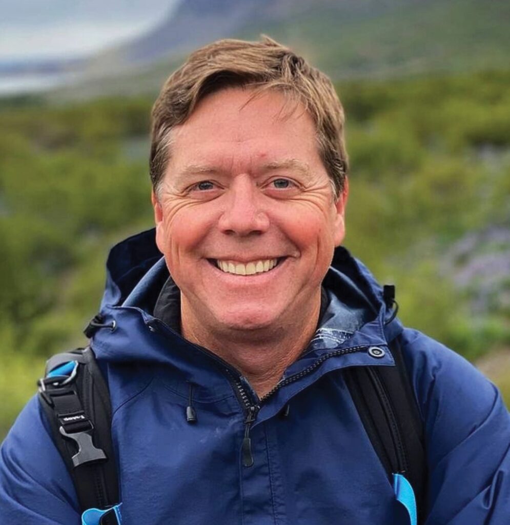 A person in a jacket with a backpack standing in front of a natural landscape.
